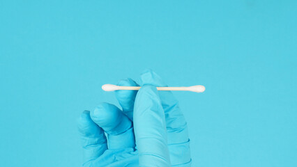 Close up of hand wears blue medical glove holding cotton bud on blue background.