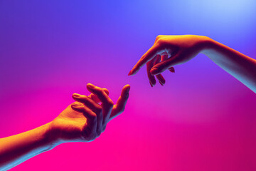 Two human hands trying to touch each other isolated on gradient blue-pink background in neon light....