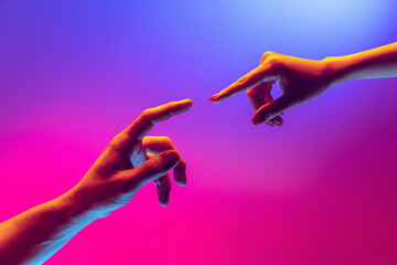 Two human hands trying to touch each other isolated on gradient blue-pink background in neon light. Concept of human relation, togetherness, symbolism, culture and history