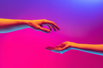 Two authentic hands trying to touch each other isolated on gradient background in neon light. Concept of relationship, community, care, support, symbolism, culture - obrazy, fototapety, plakaty