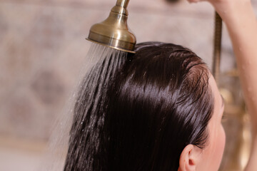 Young brunette woman washing her long hair under the shower standing with her back to the camera...