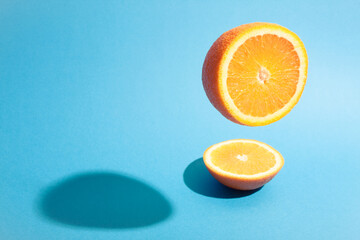 Half of orange flying on blue background with hard shadow on surface.