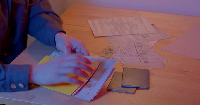 The hands of the KGB worker are looking for secret documents on the table. He decomposes and reads the necessary document. The dark world of the dark room. CZ, Kladno, Polska, 25.4.22