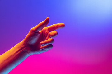 Human hand gesturing isolated on gradient purple-pink background in neon light. Concept of sign language, creativity, symbolism, culture and art