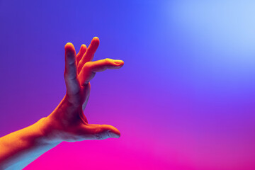 Human hand gesturing isolated on gradient purple-pink background in neon light. Concept of sign...