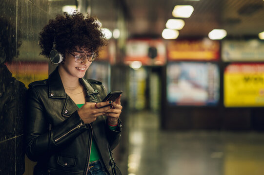 Woman in the underground metro station using smartphone and headphones