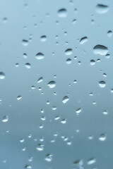 Rain drops on window glasses surface with cloudy background. Natural Pattern of raindrops isolated on cloudy background. Drops of water on glass window over blue background. 