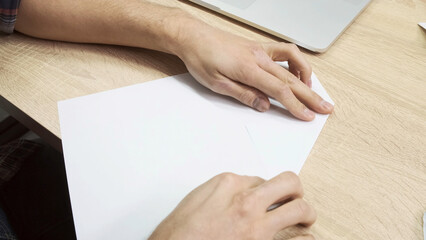Hands making origami figure. Stock footage. Close up of male hands using a white sheet of paper for making origami on wooden table background, concept of creativity.