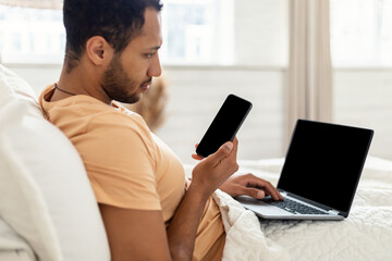 Man Using Phone And Laptop Sitting In Bed At Home