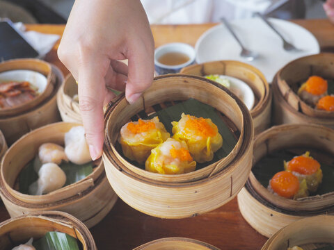 Hand holding Dim sum food in bamboo steamed basket at Chinese restaurant
