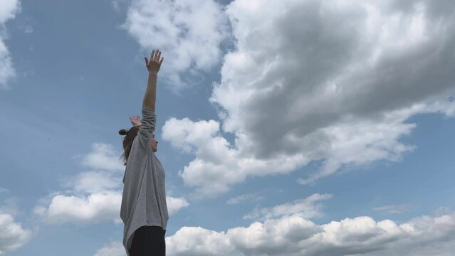Woman lifting arms overhead in namaste and doing backbend with cloudy sky as background