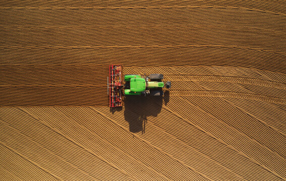 Fototapeta Aerial view of a green tractor plowing the arid soil in a paddy in the Lomellina region, Po Valley, Italy.