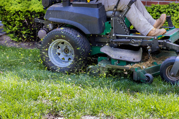 Fototapeta premium Lawn mower cutting in the grass on sunny spring day with evergreen landscaped garden
