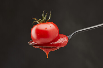Red ketchup and single tomato pouring into a spoon on a black background. Shallow depth of field	