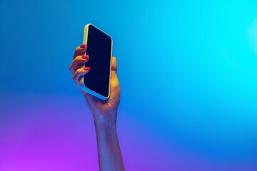 Closeup female hands holding gadget, smartphone isolated on gradient blue and purple background in...