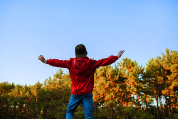 A boy in a red windbreaker jumps for joy against the backdrop of a forest.