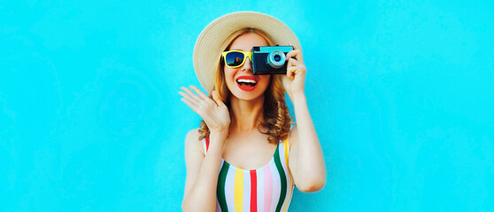 Summer portrait of happy smiling young woman photographer with film camera wearing straw hat on blue background, blank copy space for advertising text