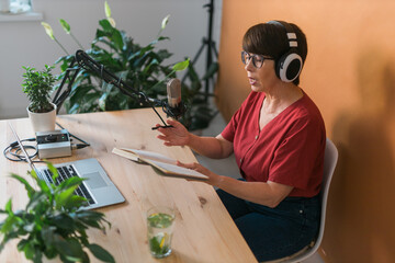 Mature woman making podcast recording for her online show. Attractive business woman using...