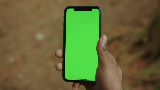 Close-up of the hand of a black man with a mobile phone with a green screen