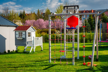 Fototapeta na wymiar Green garden with a beautiful wooden house for children and a playground at blooming spring.