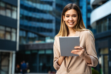 Portrait of a successful business woman using digital tablet in front of modern business building - obrazy, fototapety, plakaty