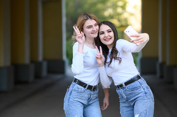 Young brunette and blonde girls take a selfie on the street.