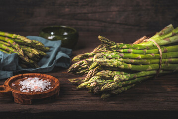 Green spring asparagus cooking preparation.   Springtime asparagus bunch on dark rustic kitchen...
