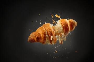 Falling delicious fresh baked croissant on black background. French pastry