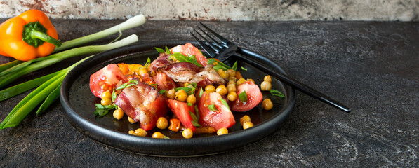 plate with salad with chickpeas, bacon, peppers and tomatoes on a dark table