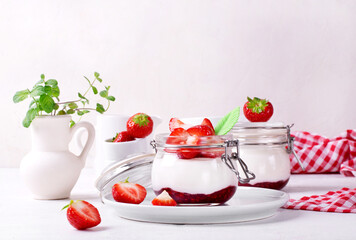 Yogurt with raspberry jam in the jar topped with strawberries on the white table. Healthy breakfast. Copy space