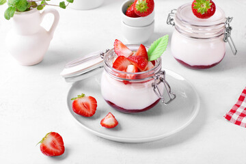 Yogurt with raspberry jam in the jar topped with strawberries on the white table. Healthy breakfast