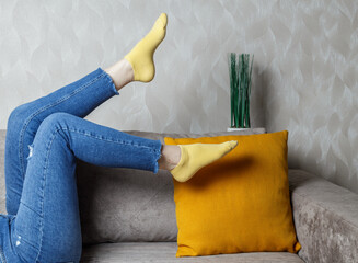slender female legs in jeans and yellow socks on the sofa. Light sofa and orange pillow.
