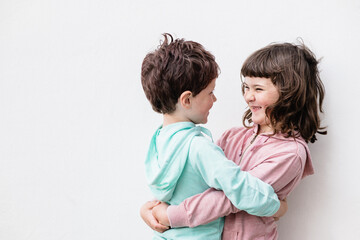 Happy siblings hugging near white wall