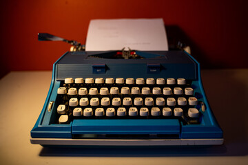 Photo of a vintage blue typewriter on a white table and an orange color wall