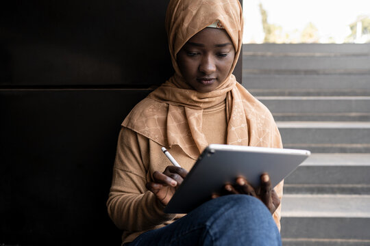 Serious Black Lady In Hijab Browsing On Tablet On Street