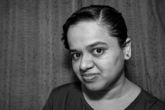 Grayscale Shot Of A Cheerful South Asian Woman From India Standing In Front Of A Curtain