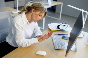 Businesswoman sitting at workplace in office touch to wrist and feels pain