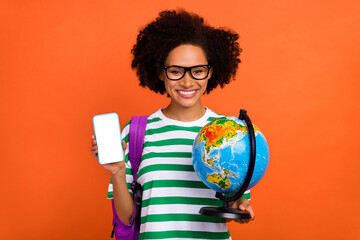 Portrait of beautiful trendy cheerful girl holding globe find point place tour using device gps isolated on bright orange color background