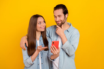Photo of impressed young brown hairdo couple look telephone wear jeans shirt isolated on yellow background