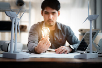 Energy engineer holding light bulb in modern office with solar cell sample and wind turbine model, Creative thinking innovative alternative energy design. Saving nature or ecology concept.