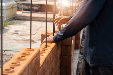 Fototapeta premium Builder carefully puts red brick on the masonry. Quick work bricklayer. Guy measures level masonry. Man is building brick wall. Correctly calculate material. Builder manually carries brick structure