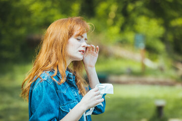 Young woman sneezing in park. Allergy, flu, virus concept. Spring allergy concept. Young woman...