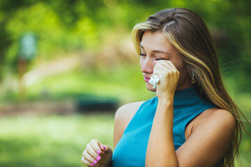 Young woman sneezing in park. Allergy, flu, virus concept. Spring allergy concept. Young woman suffering from allergy outdoors. Young woman with Pollen allergy