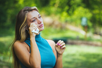 Young woman with pollen and grass allergies. Flowering trees in background. Spring Seasonal...