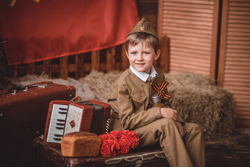 a smiling child boy in a soldier's suit with a cap in the military-patriotic zone dedicated to...