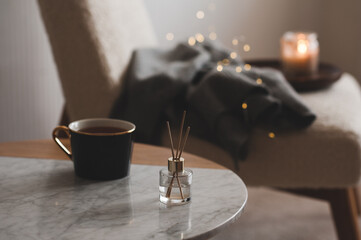Bamboo sticks in bottle with scented candles and cup of tea on marble table closeup. Home aroma. Aromatherapy. Apartment living.