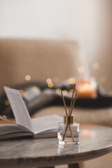 Bamboo sticks in bottle with scented candles and open book on marble table closeup. Home aroma....