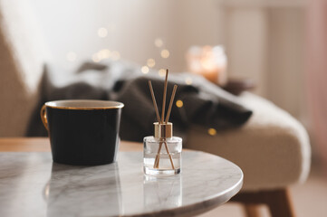 Bamboo sticks in bottle with scented candles and cup of tea on marble table closeup. Home aroma....