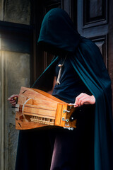 Closeup of a man in a cloak holding a hurdy gurdy medieval instrument