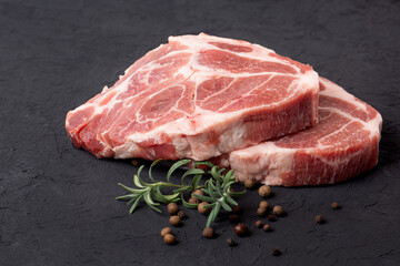 Steaks of raw marbled pork tenderloin on a black background with rosemary and peppercorns.